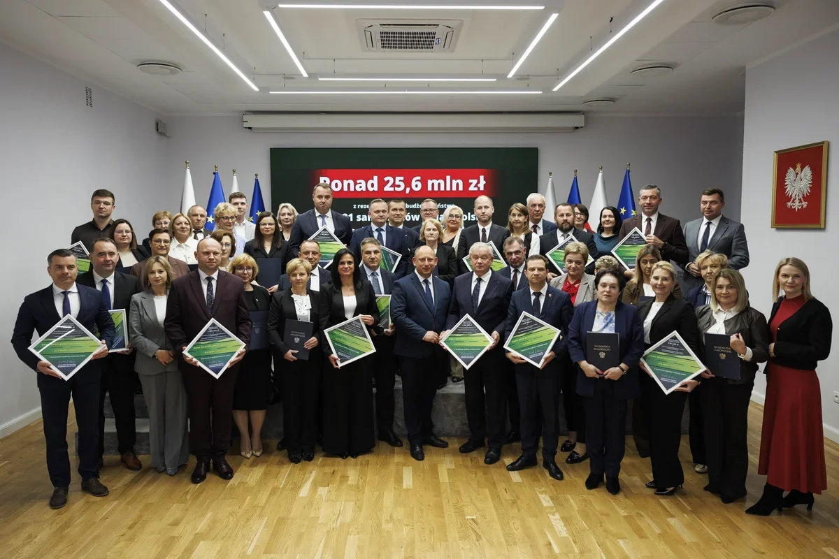 Grupa osób w formalnym stroju stoi w sali konferencyjnej z dyplomami podczas uroczystości wręczenia wsparcia finansowego dla sądów.