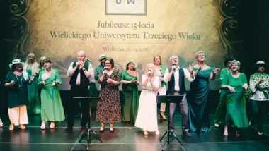 Grupa osób występuje na scenie podczas jubileuszu 15-lecia Wielickiego Uniwersytetu Trzeciego Wieku w Wieliczce.