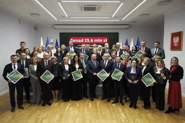 Grupa osób w formalnym stroju stoi w sali konferencyjnej z dyplomami podczas uroczystości wręczenia wsparcia finansowego dla sądów.